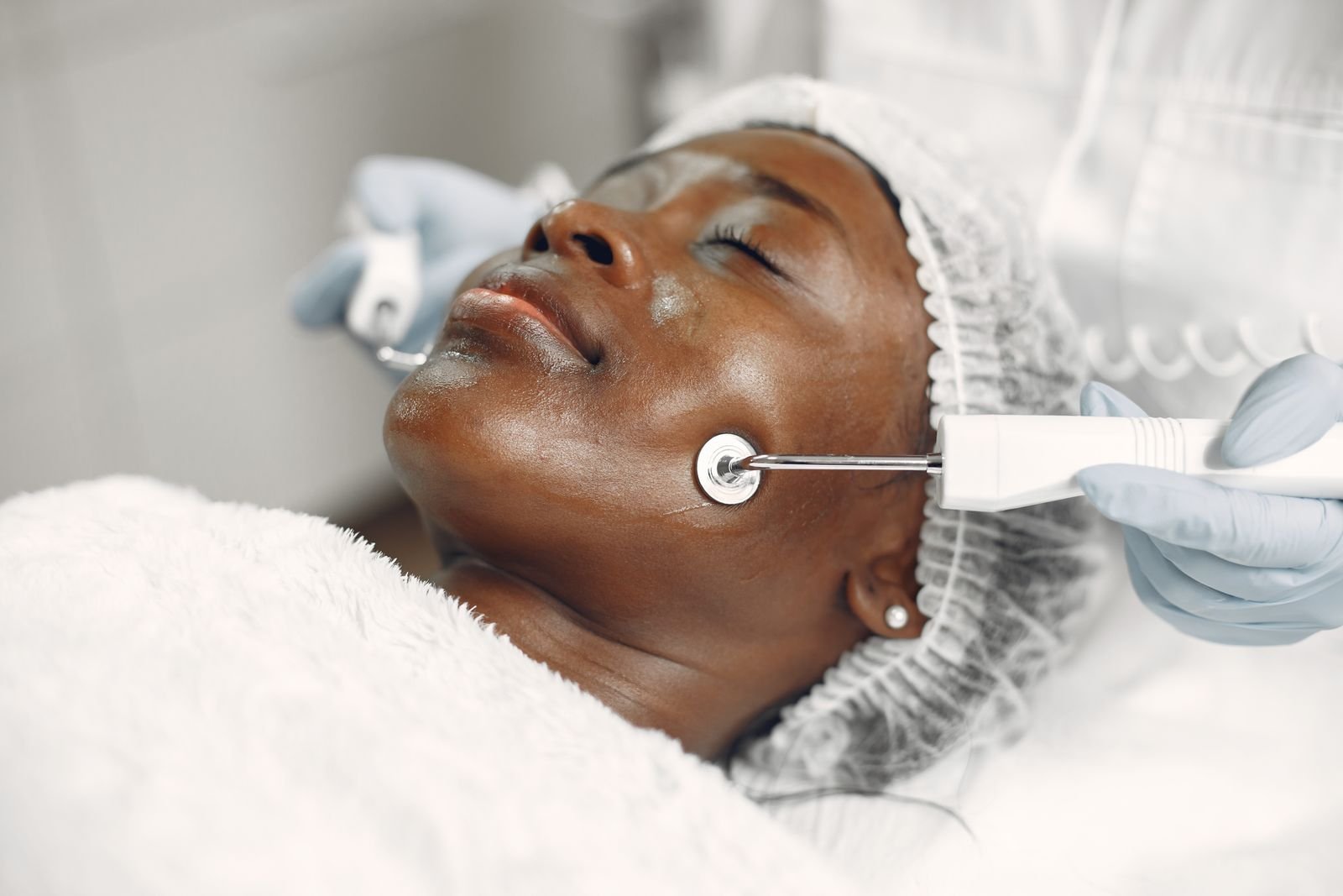 alta frequência facial: profissional de luvas aplica aparelho facial no rosto da cliente em cabine