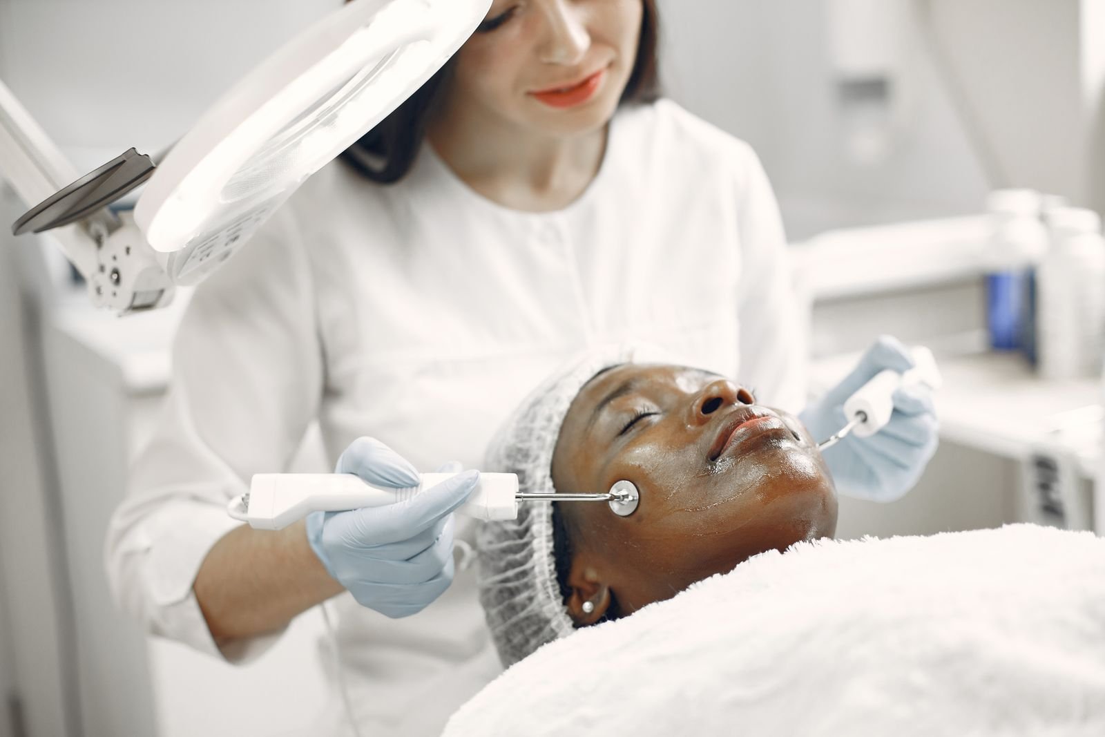 esteticista aplicando aparelho facial com dois eletrodos em cabine iluminada