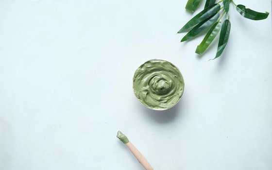 Profissional aplicando argila no rosto da cliente durante protocolo detox
