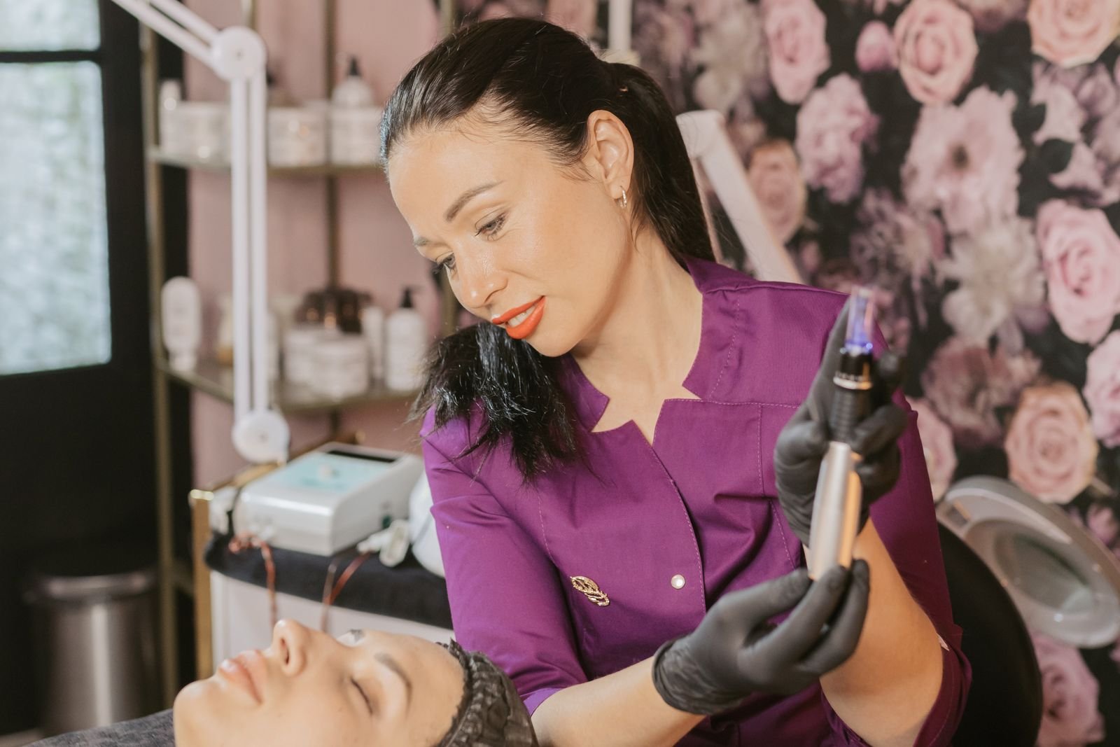 esteticista de luvas segurando aparelho facial em cabine com lupa e prateleira de produtos