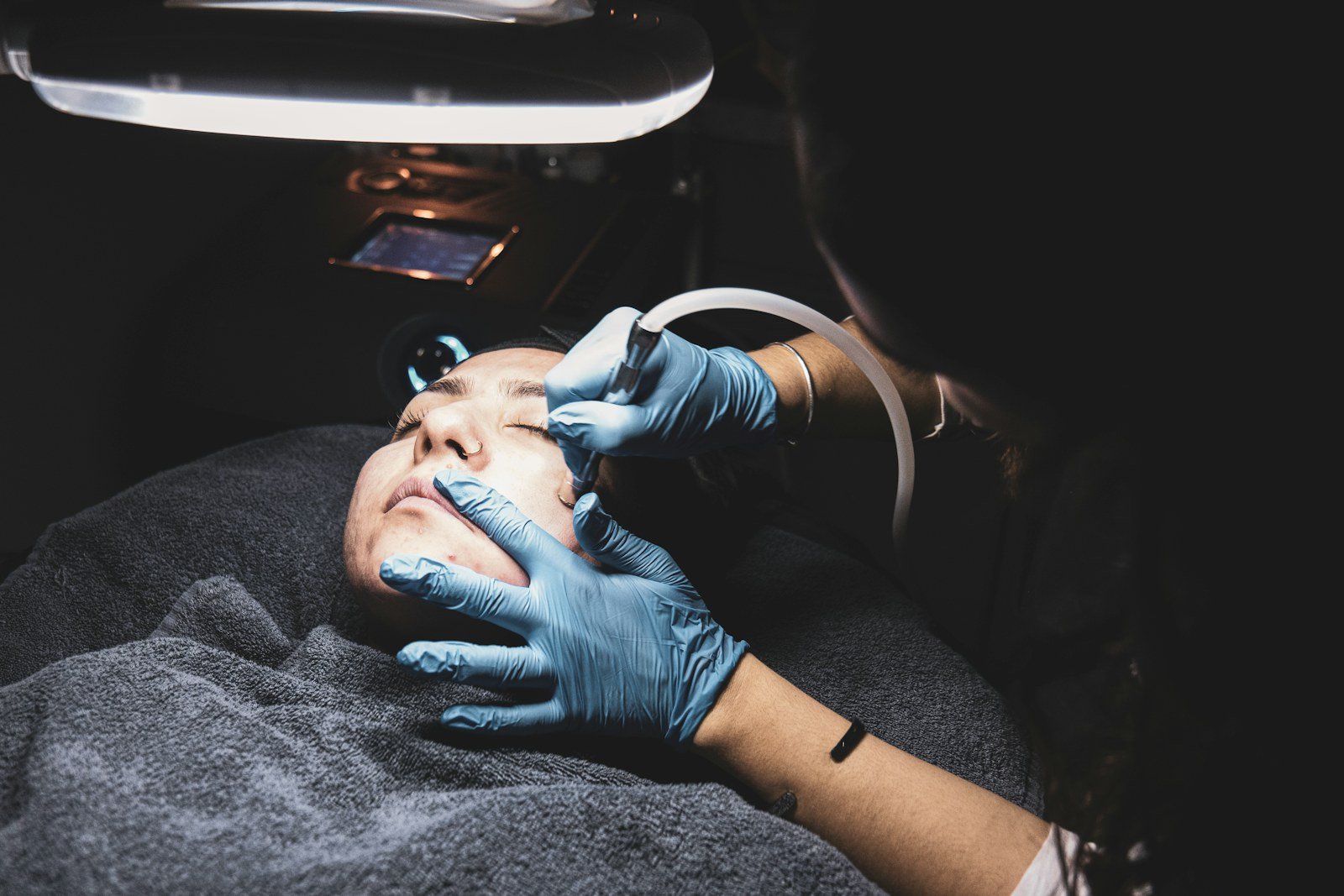 Extração de cravos com profissional de luvas atendendo o rosto de uma cliente na maca