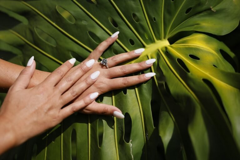 Mão com manicure branca e anel, mostrando o formato das unhas