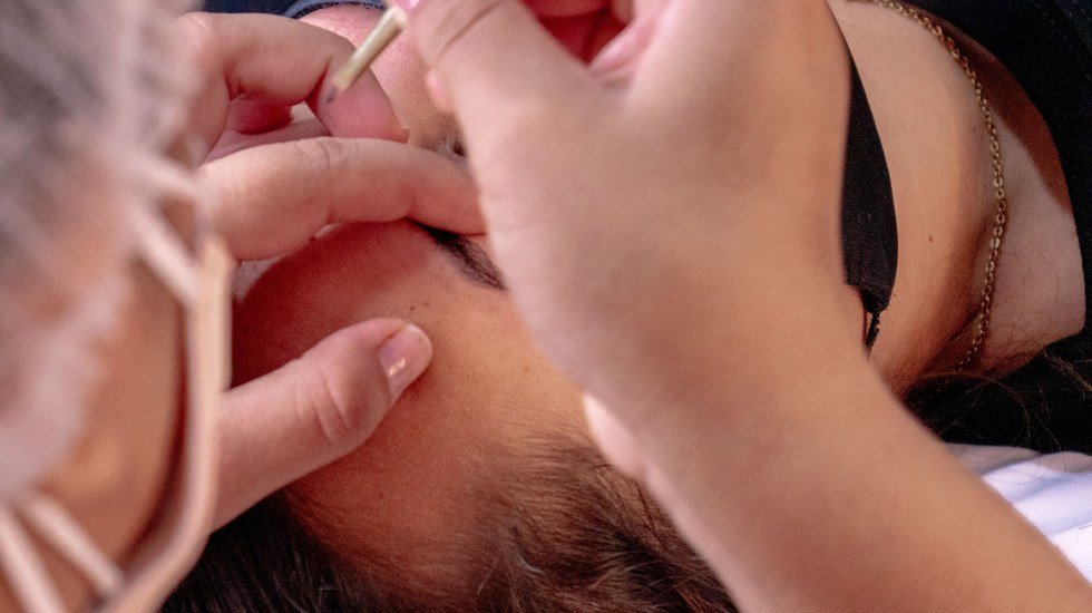 Profissional aplicando henna na sobrancelha de uma cliente durante procedimento de design