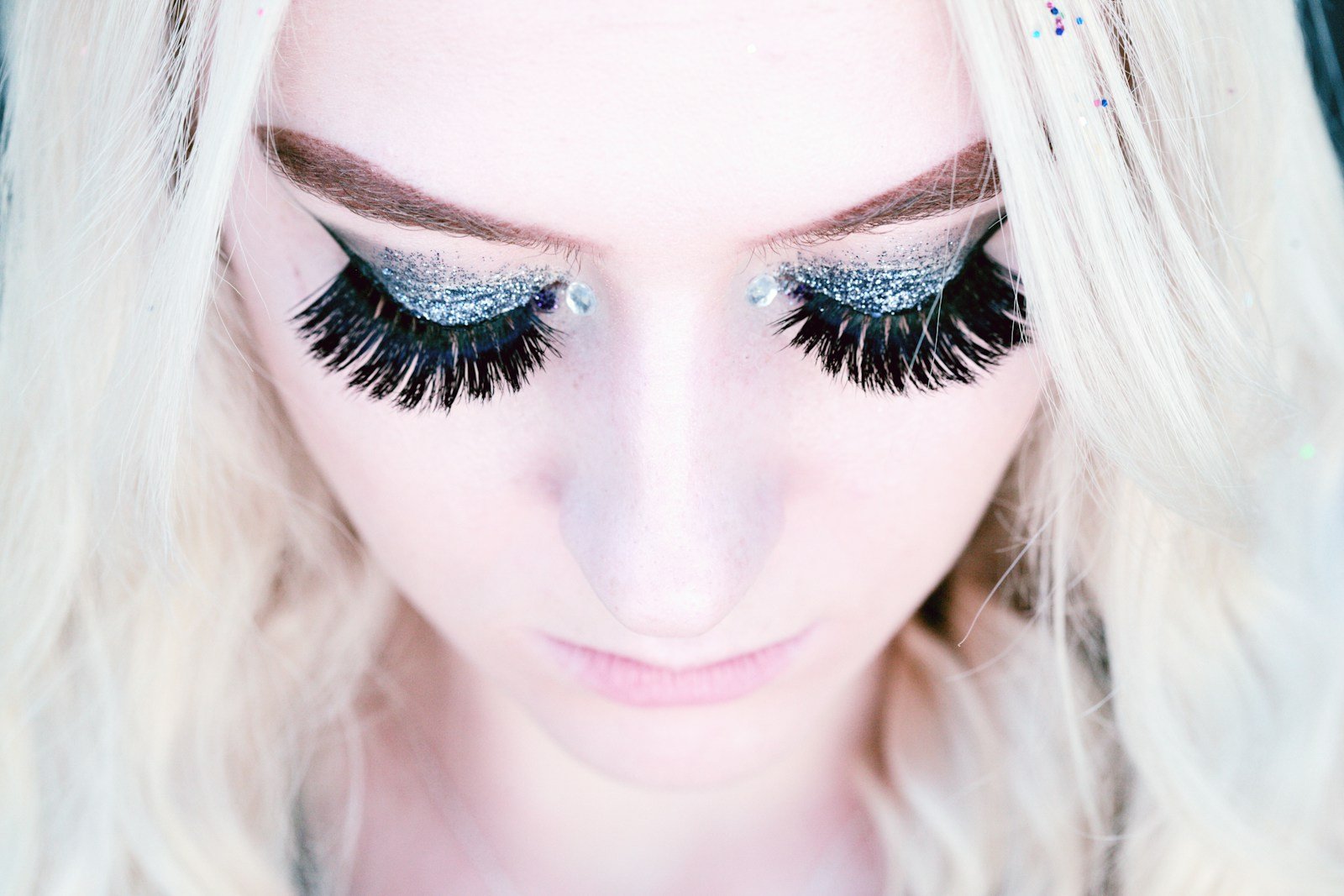 Mulher de olhos fechados com cílios volumosos e maquiagem com glitter para festa