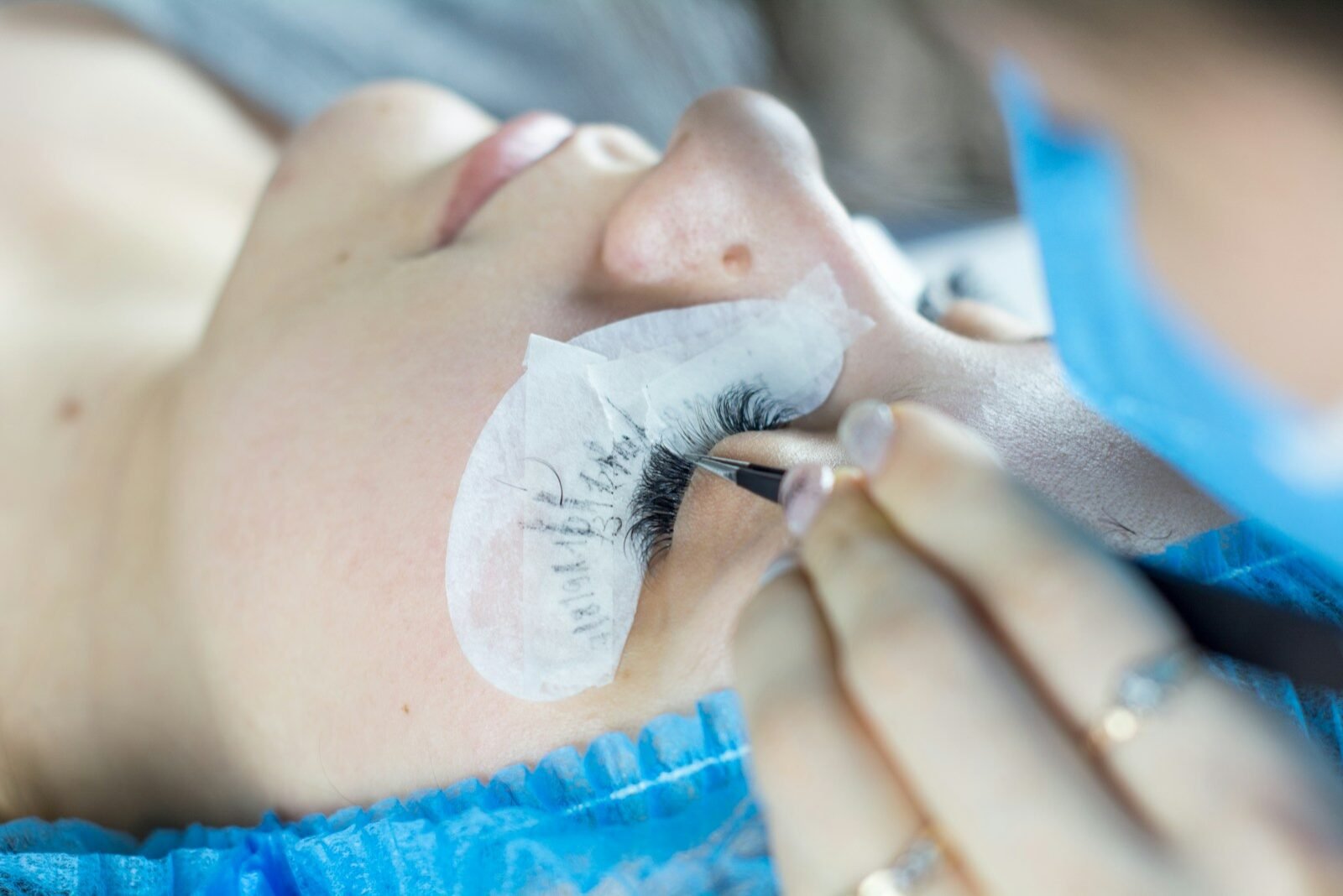 Profissional aplicando extensão de cílios com pinça em cliente com protetor de gel sob os olhos