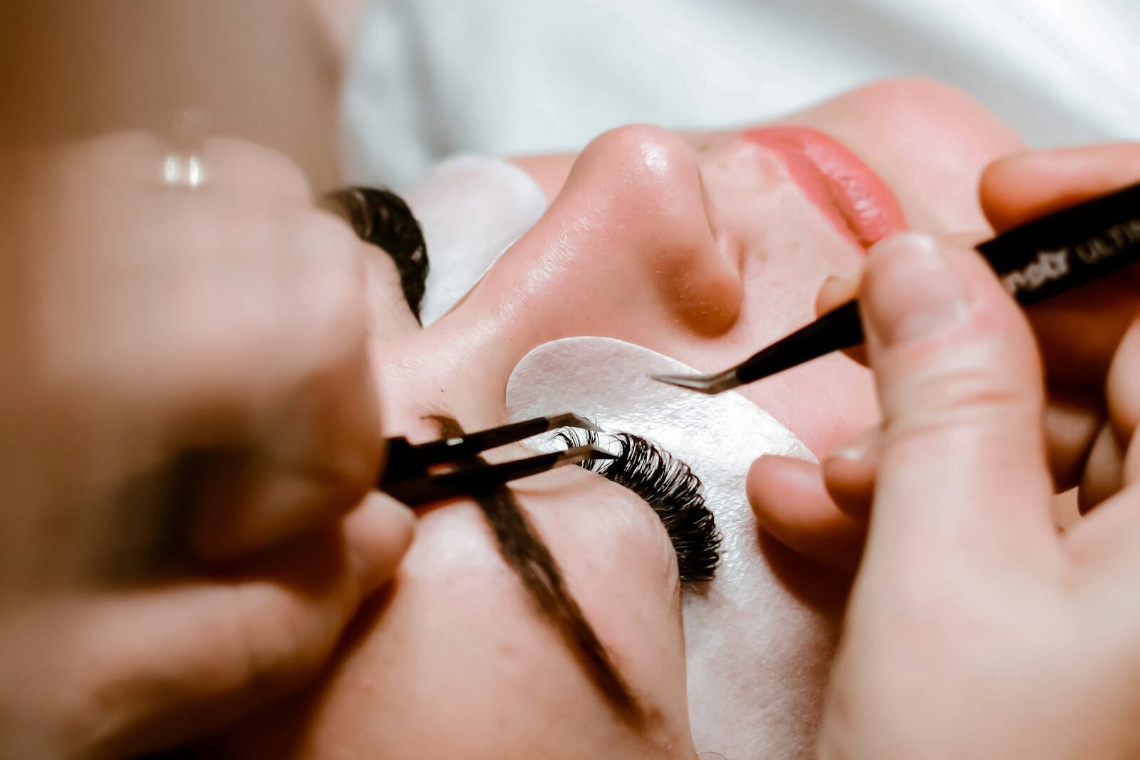 Lash designer aplicando extensão de cílios fio a fio com pinça em cliente deitada