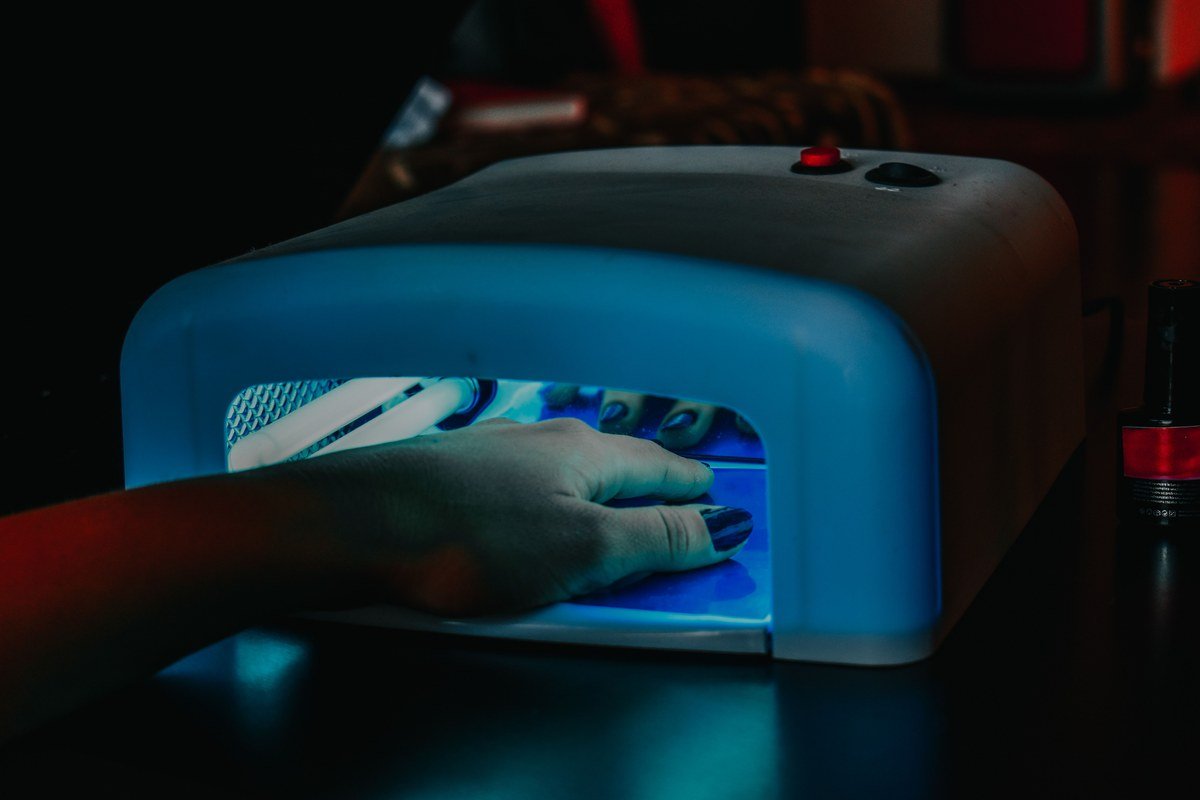 Mão em cabine de LED curando esmaltação em gel, técnica ensinada no curso de unha de gel da Nail Academy