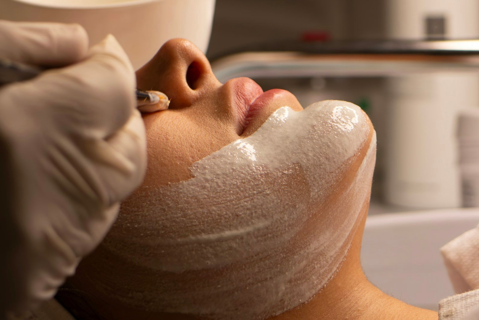 Esteticista de luvas aplicando máscara facial com espátula durante a sessão