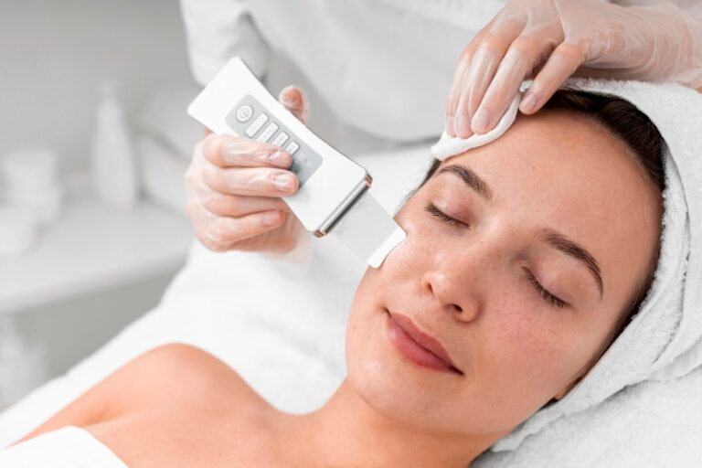 Esteticista passando aparelho facial no rosto de uma cliente deitada, de olhos fechados, em cabine de estética