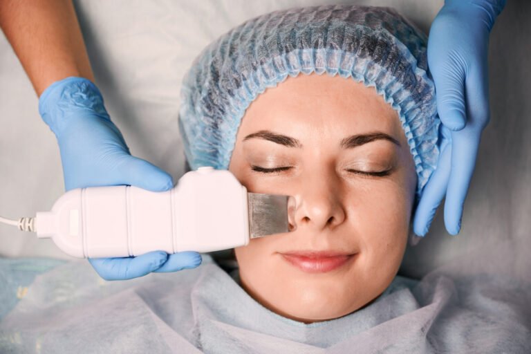 Profissional de luvas passando espátula ultrassônica no rosto de uma cliente, um dos tipos de limpeza de pele