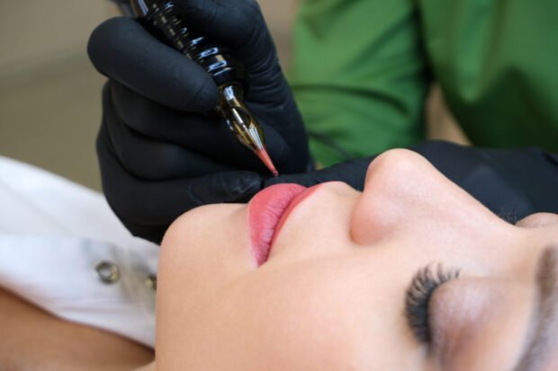 Close do dermógrafo aplicando pigmento no lábio de uma cliente durante a micropigmentação labial