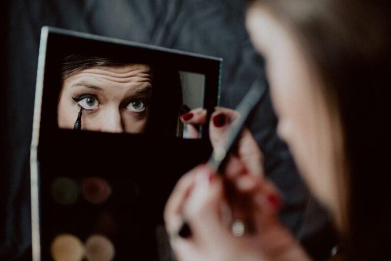 como fazer delineado: mulher aplicando delineador líquido preto com espelho na mão