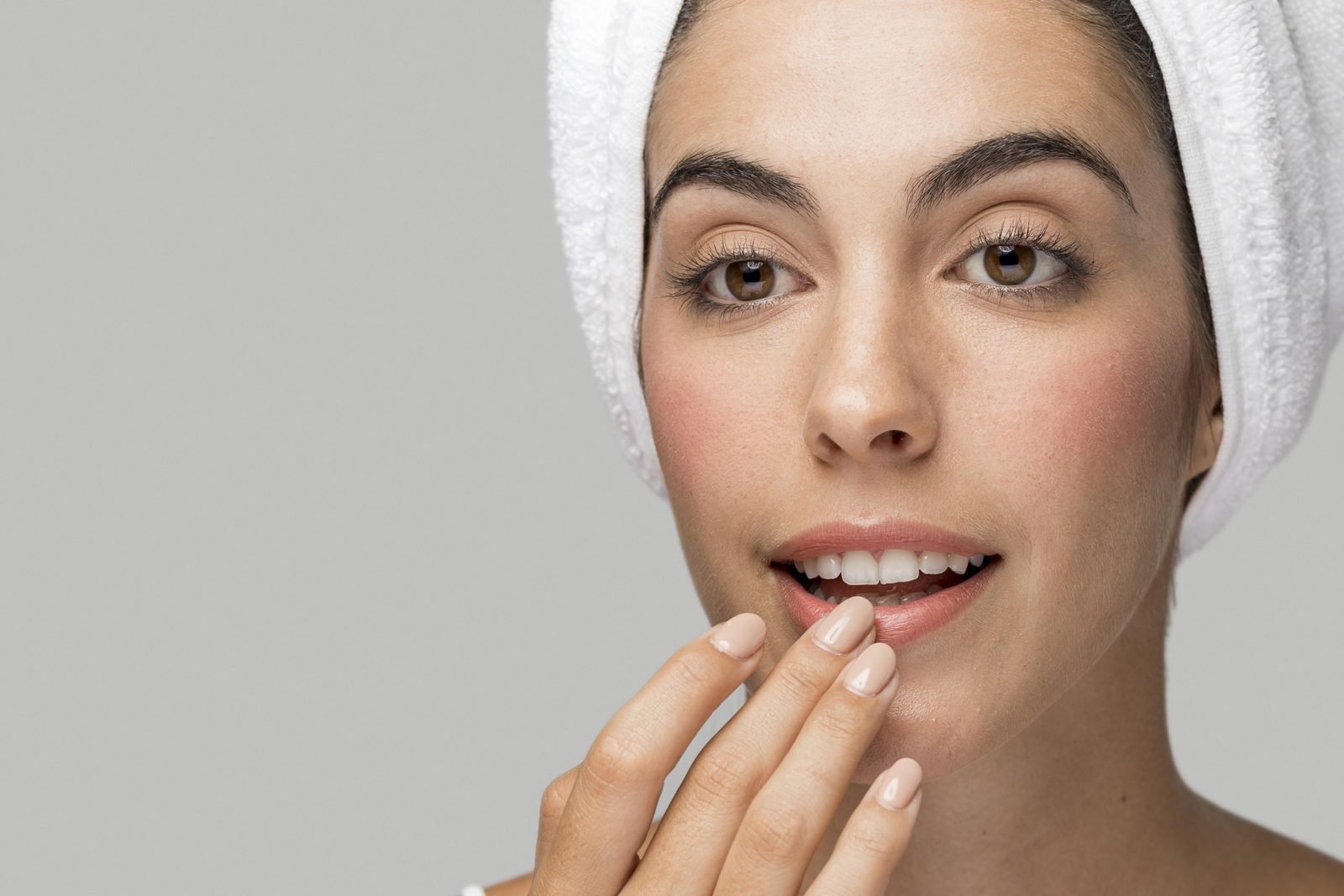 mulher com toalha no cabelo hidratando os lábios com a ponta dos dedos nos cuidados pós micropigmentação labial