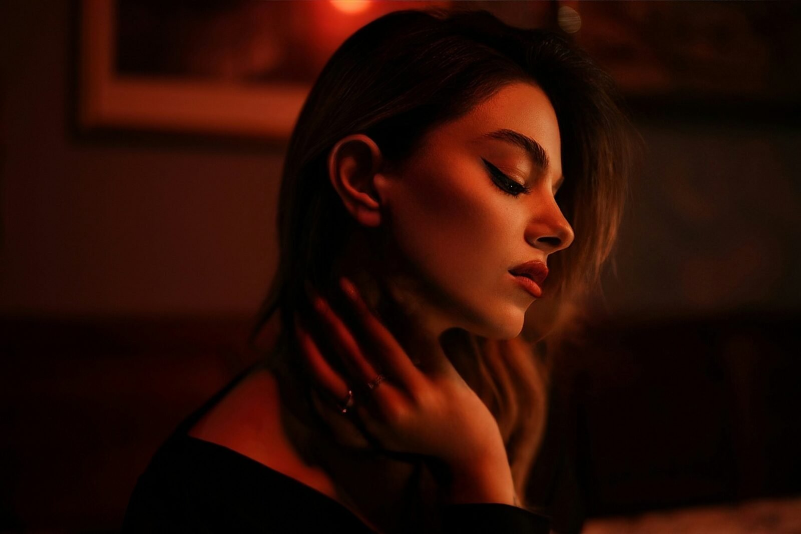 mulher com maquiagem simples para noite, delineado fino e batom vermelho, em luz baixa e quente